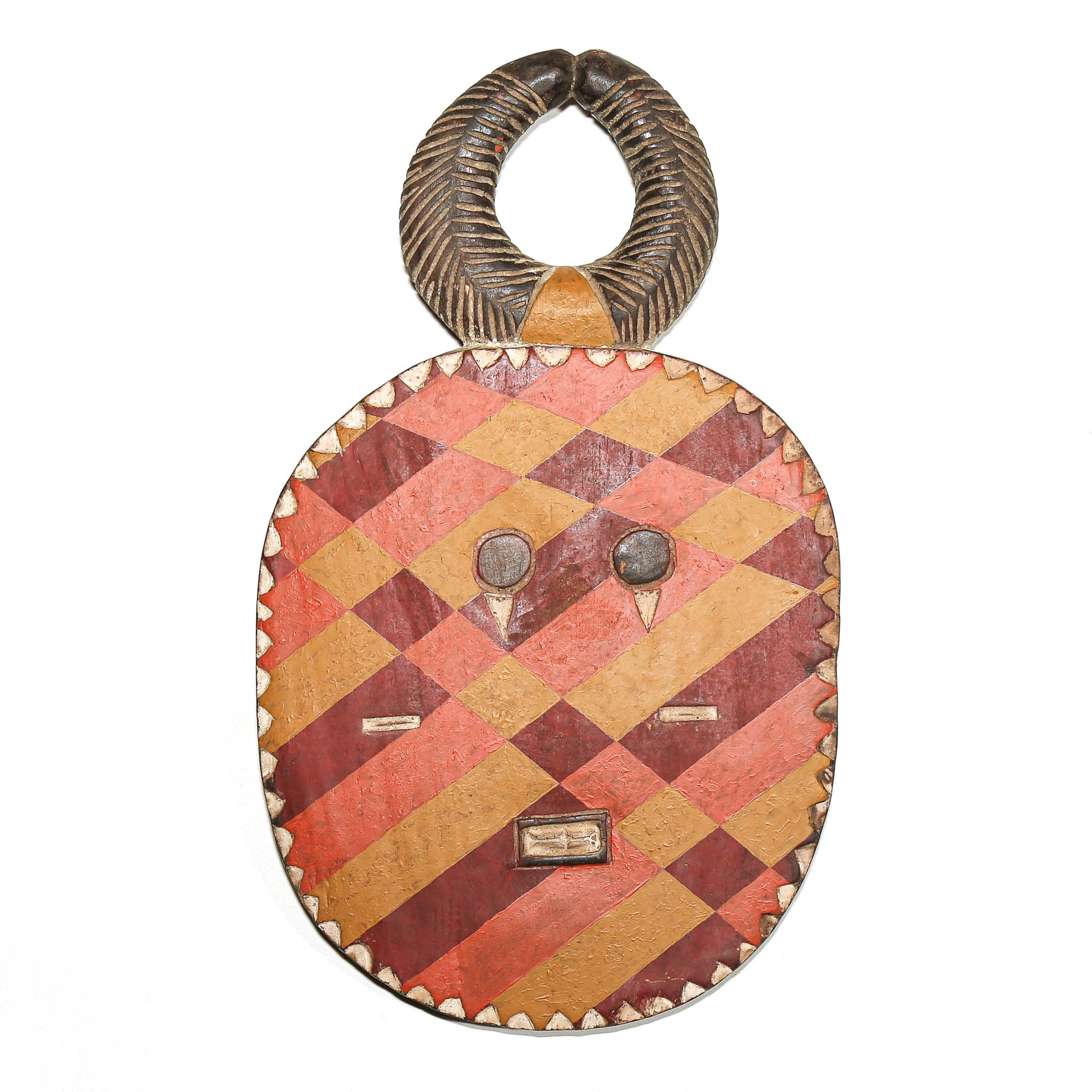 A carved wooden African-style mask or decorative plaque with a loop handle, featuring a diamond-pattern face in orange, red, and tan tones with small dark eyes and a carved top section.