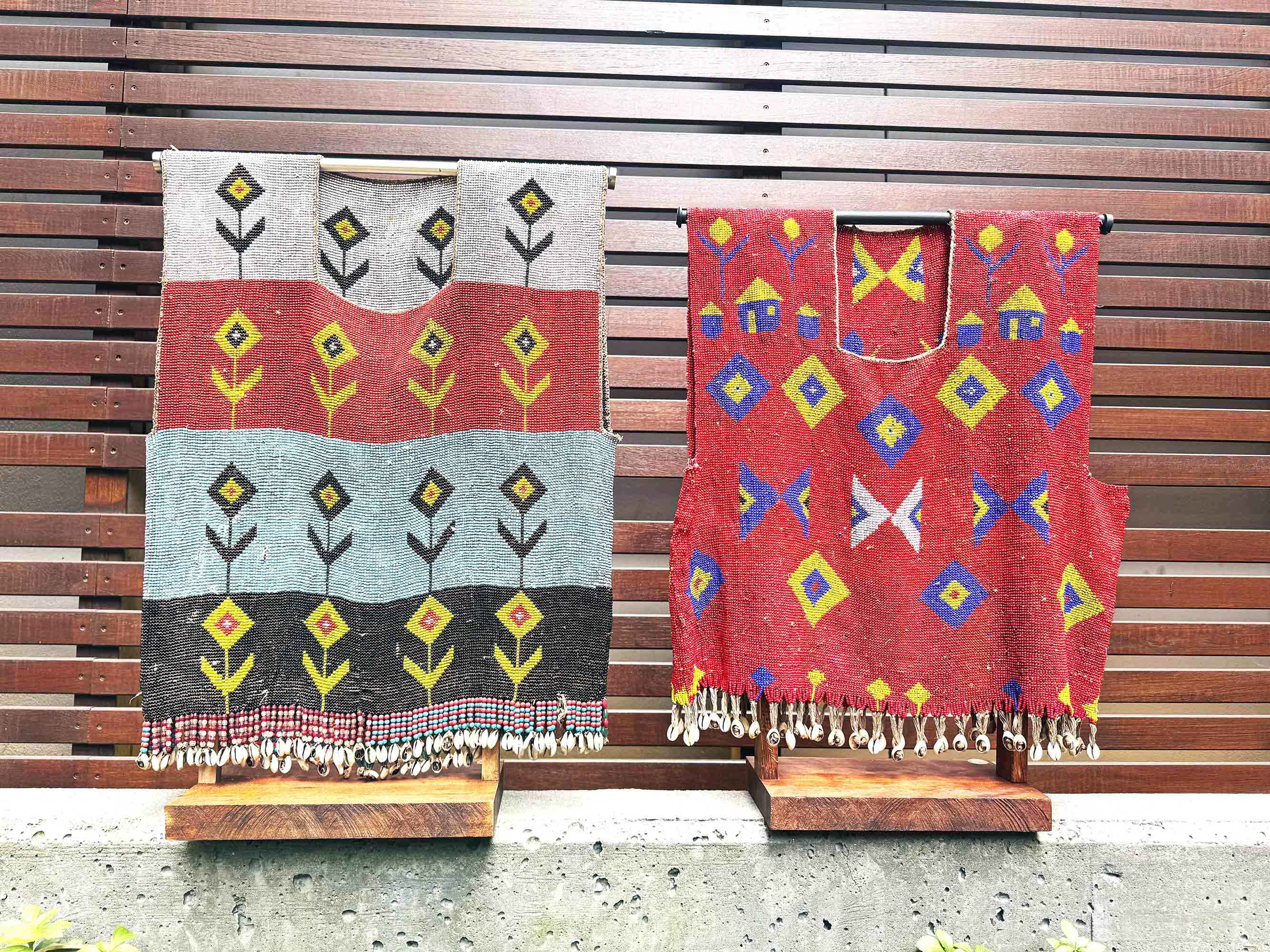 Two patterned vintage shirts from cameroon africa on stands against a wooden slat background