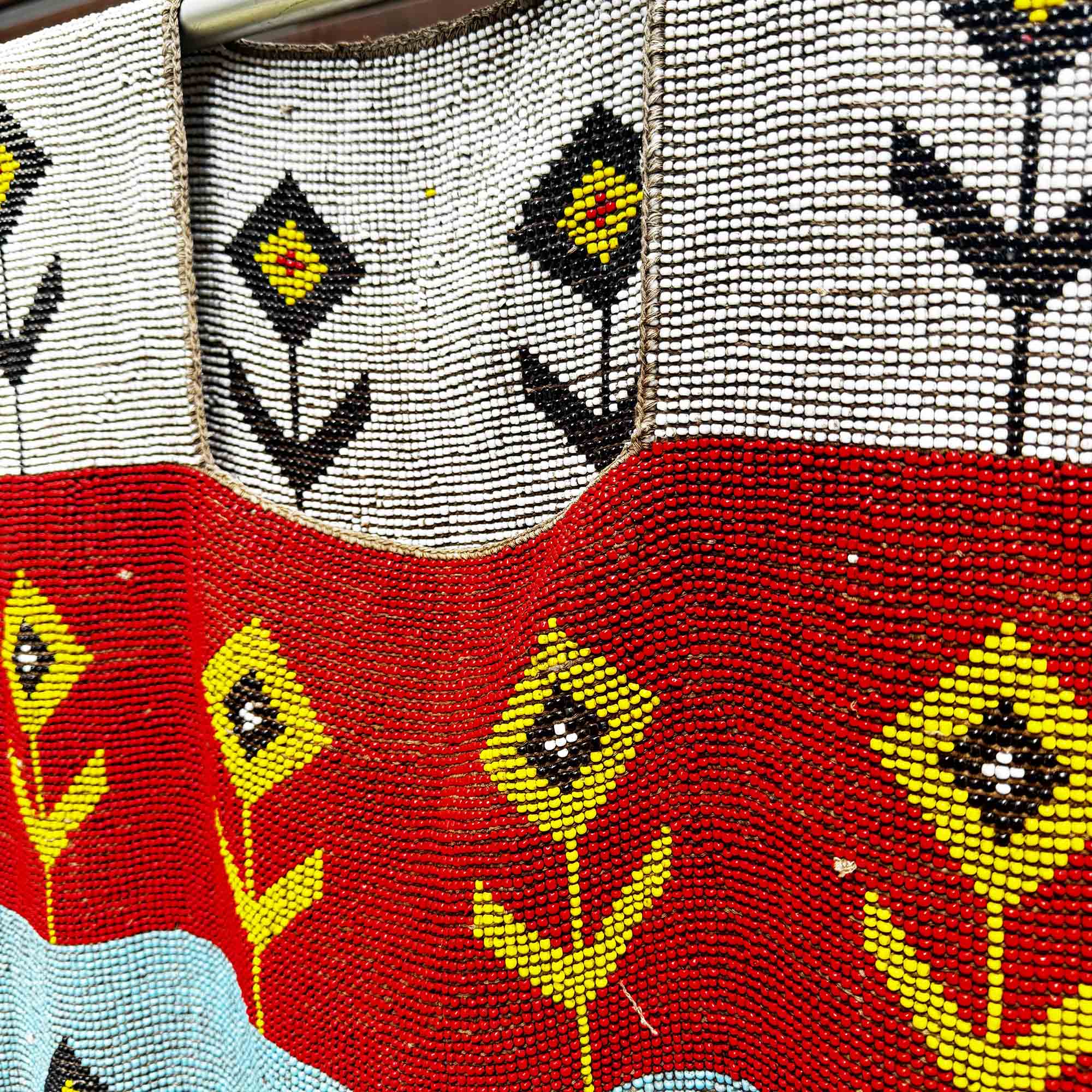 Close-up of a beaded african fabric with floral patterns in red, yellow, and black on a white background.