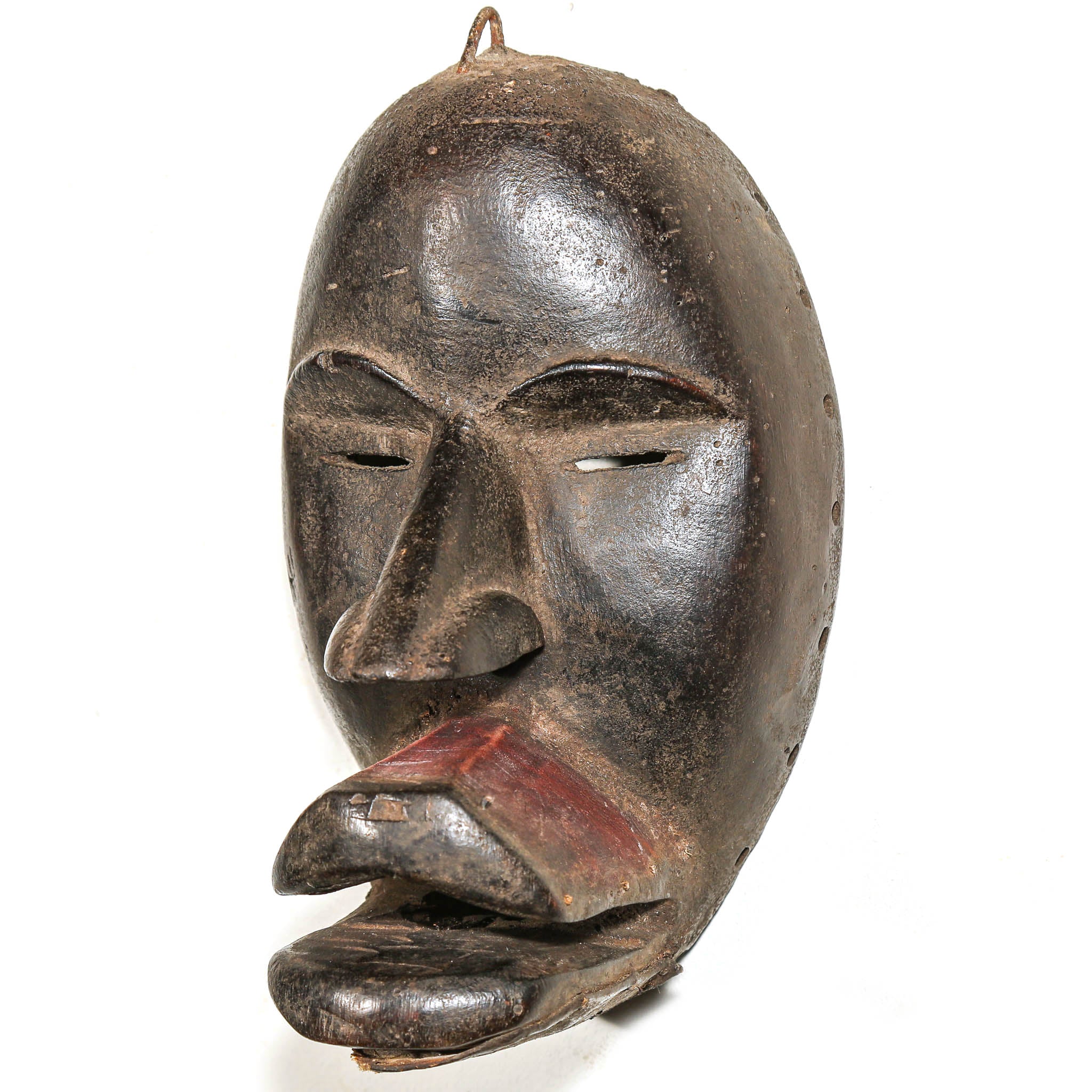 A black carved wooden mask with a protruding tongue, photographed against a plain white background.