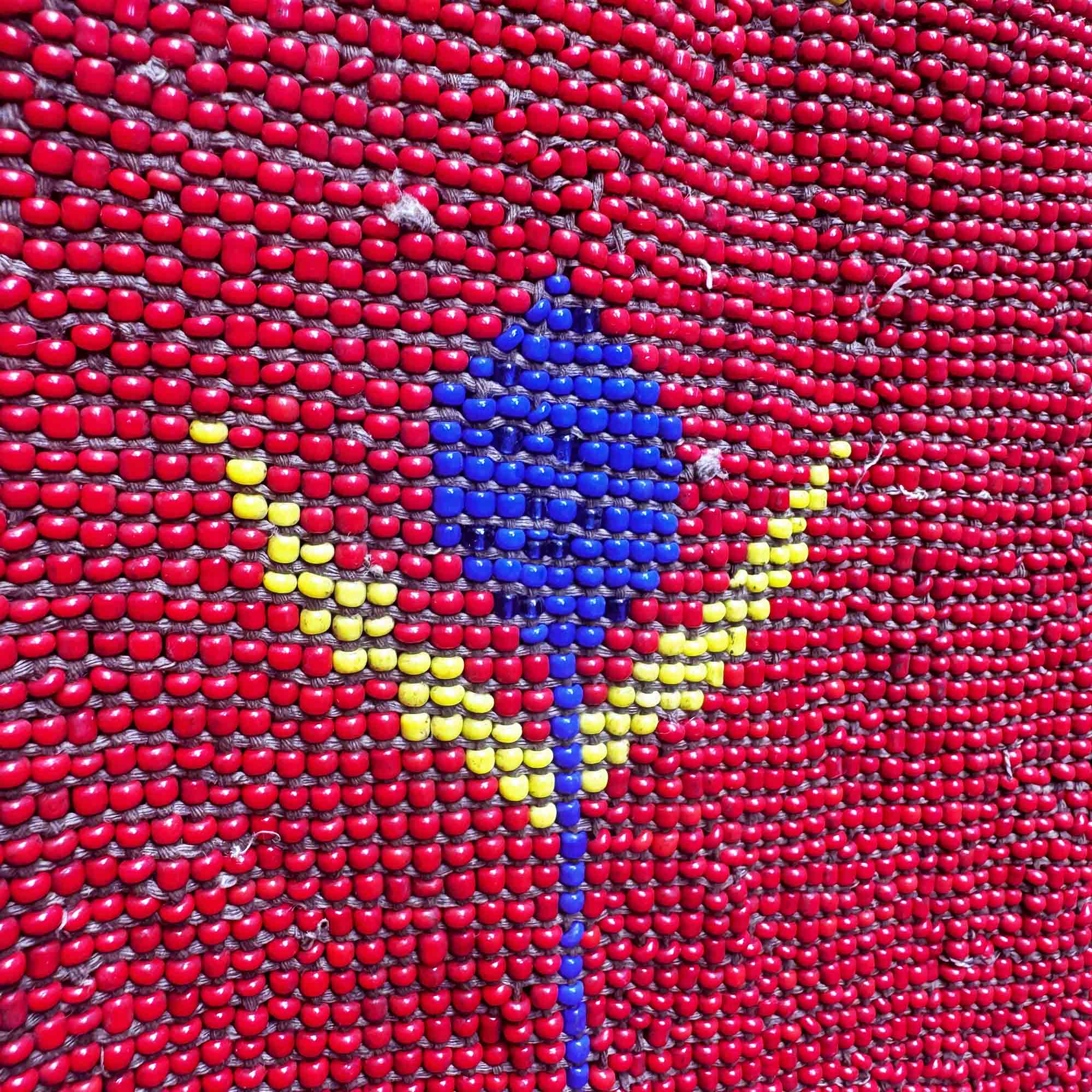Close-up of a beaded design with red, blue, and yellow colors on a textured background.