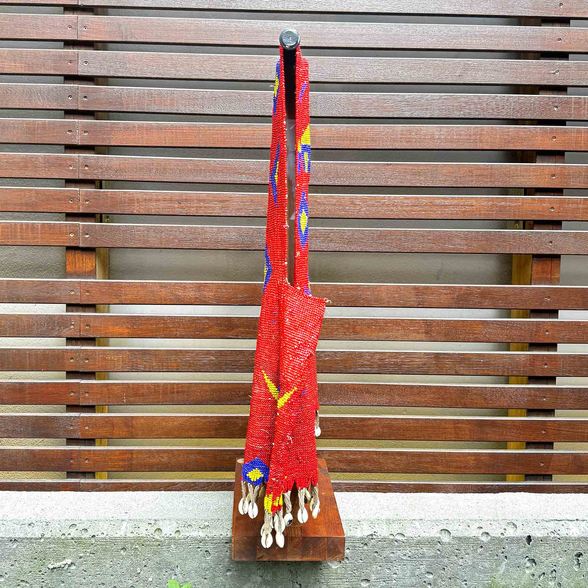 Red african beaded fashion with colorful patterns hanging on a wooden slat wall.