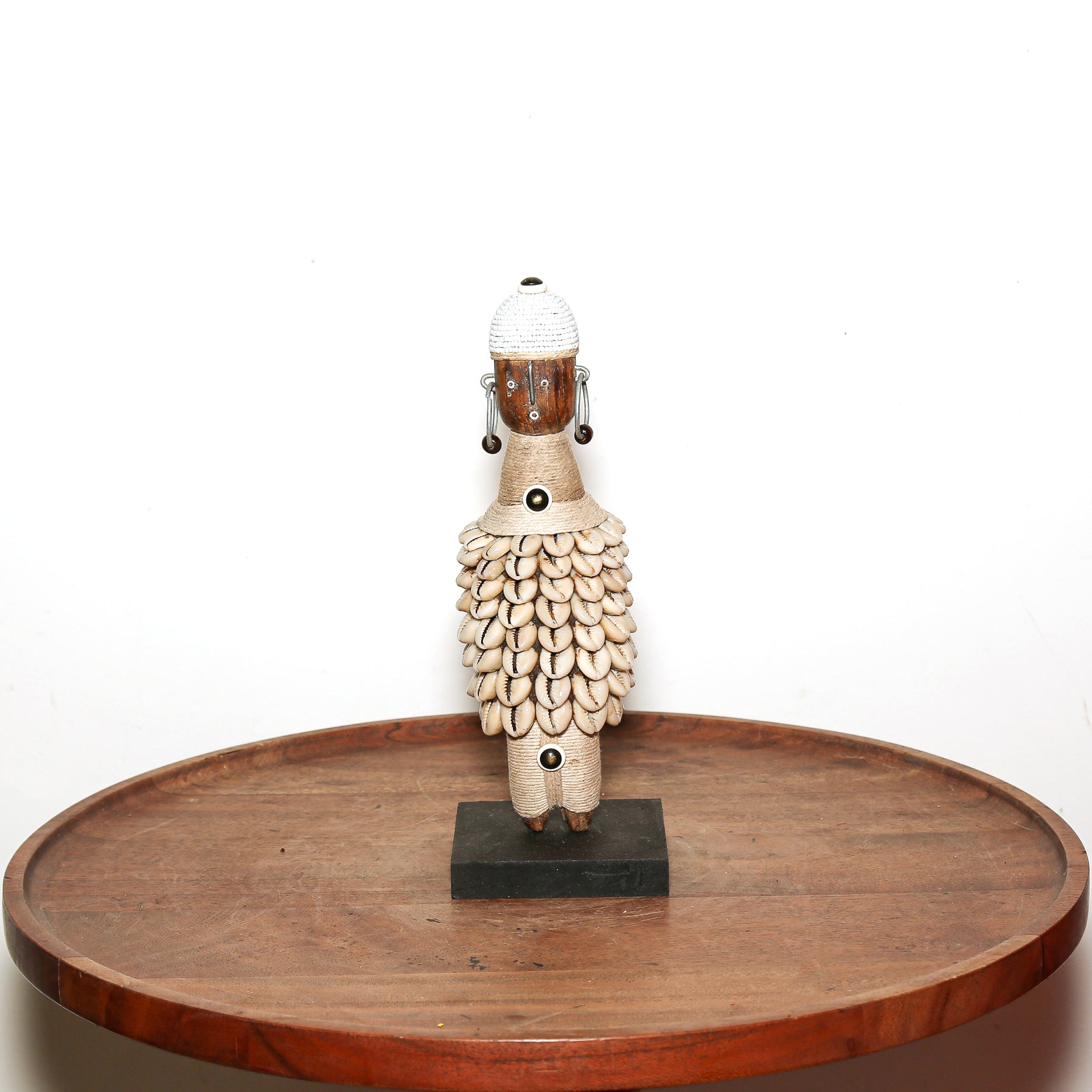 A hand-carved African wooden figurine of a sheep, displayed on a round wooden tray against a plain white background.