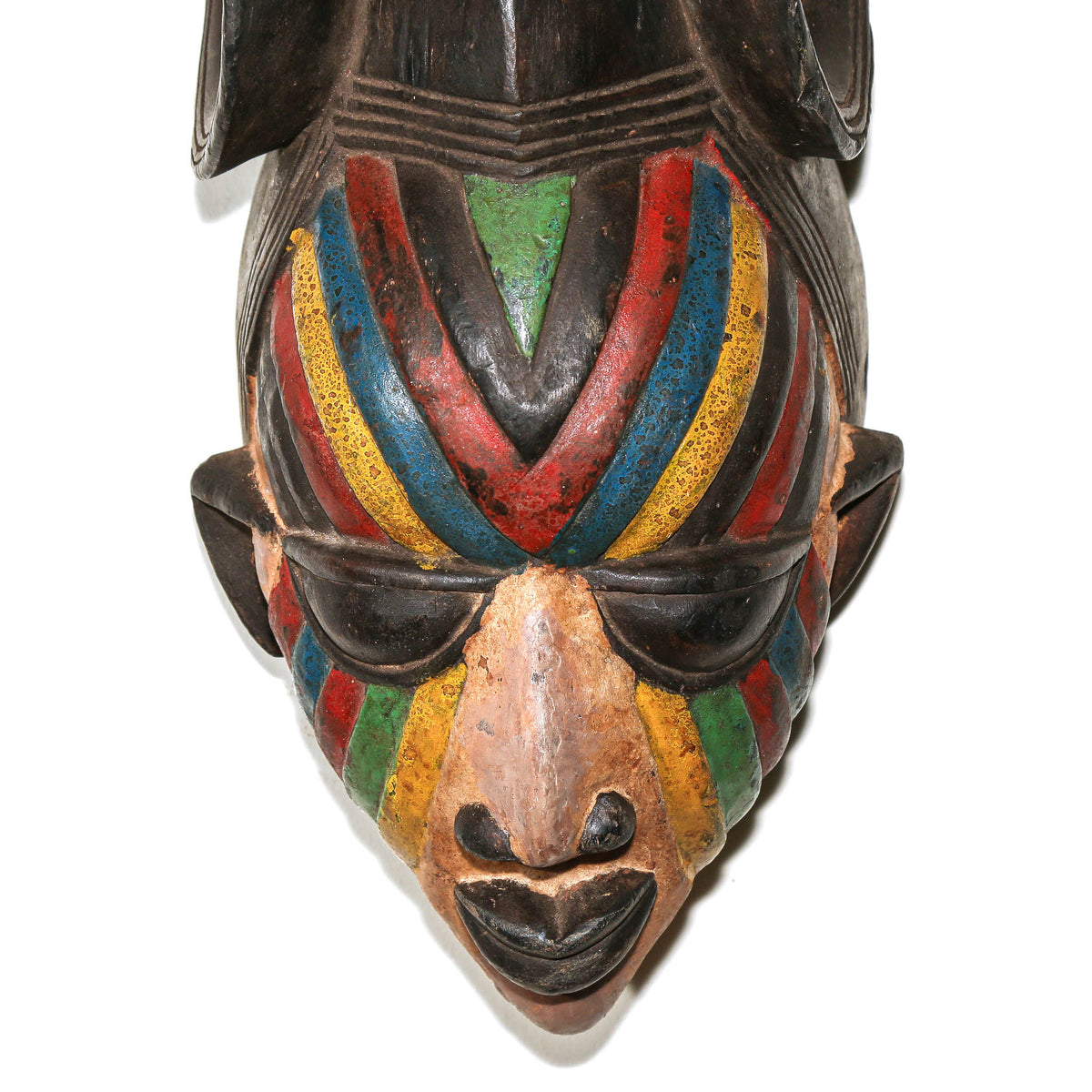 A close-up of a carved wooden mask head with a dark base and vibrant painted stripes in red, yellow, blue, and green across the face, shown against a plain white background.